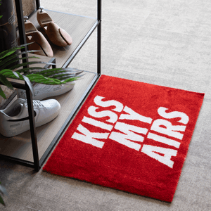a red rug with white text on it next to a plant and shoes